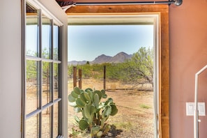 Enjoy breathtaking views of the desert landscape from this room's large window, featuring a cactus plant and distant mountains.