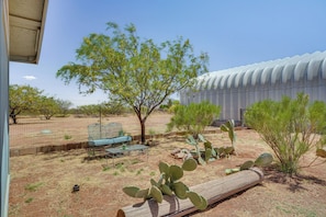 Relax in a serene desert oasis with a bench and table for unwinding amidst lush cacti and trees.
