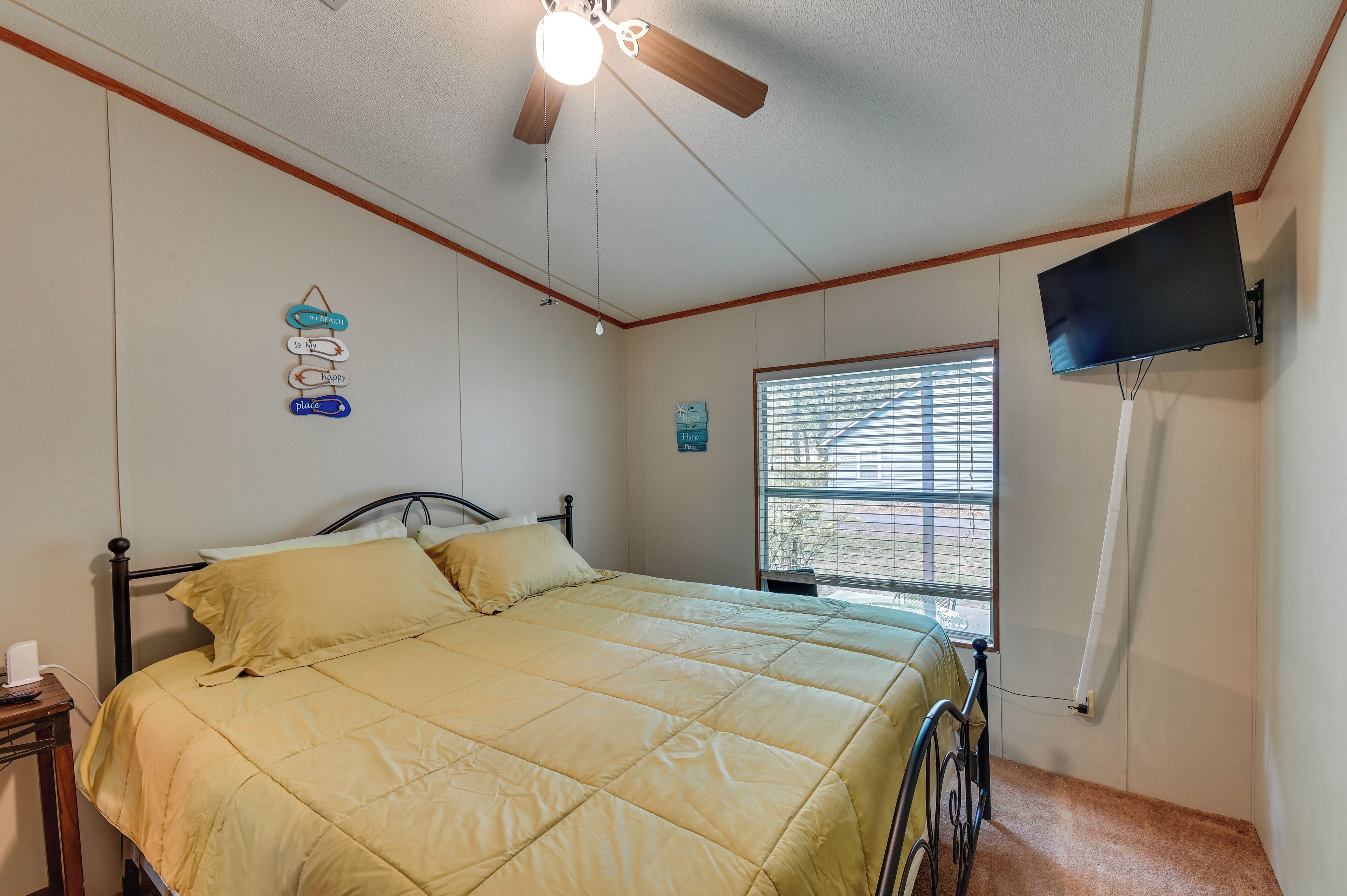 A bedroom with a bed, a ceiling fan, a mounted TV, and a window with blinds.