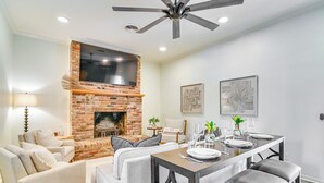 Una sala de estar moderna con chimenea de ladrillo, una mesa de comedor para cuatro comensales y un ventilador de techo.