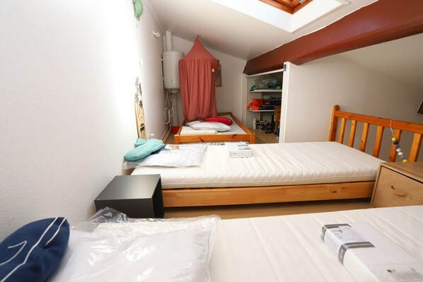 Ein kleiner, gut beleuchteter Raum mit einem Oberlicht, einem hölzernen Bett, einem Nachttisch und einem Kleiderschrank mit Regalen.
