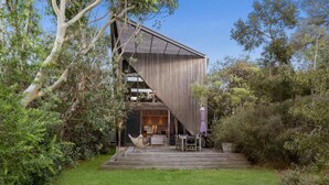 A modern house with a large wooden deck, a dining area with outdoor furniture, and a kitchen visible through a glass door. - Aireys Cliff-Top Gem - Your Ultimate Coastal Escape (Aireys Inlet)
