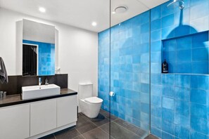 Un baño moderno con un lavabo blanco, un inodoro y una zona de ducha con azulejos azules.