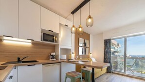 Eine moderne Küche mit Holztresen, integriertem Mikrowellenherd und einer Kaffeemaschine. Es gibt einen Essbereich mit Tisch und Stühlen sowie ein großes Fenster mit Blick auf die Stadt.