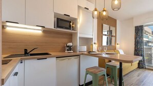 Eine moderne Küche mit weißen Schränken, einer Mikrowelle, einer Kaffeemaschine und einem Essbereich mit einem Holztisch und grünen Hocker.