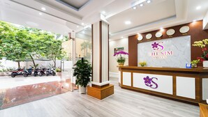 A hotel reception area with a marble reception desk, a clock displaying time in multiple cities, and a view of parked motorcycles outside.