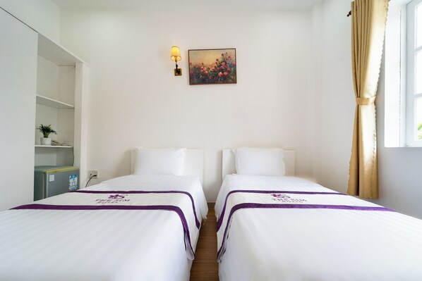 Habitación de hotel con dos camas, un escritorio pequeño, una lámpara y un cuadro en la pared.