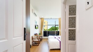 Hotelkamer met twee bedden, een bureau, een stoel en een raam met uitzicht op gebouwen en groen.