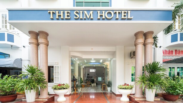 De ingang van The Sim Hotel, met een statig gevel, grote zuilen en plantenpotten.