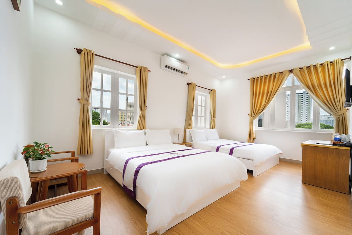 A hotel room with two beds, a desk, a chair, and a potted plant.