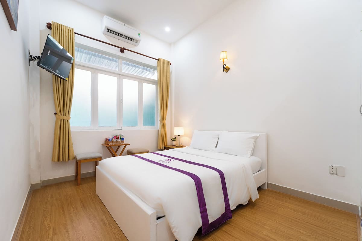 A hotel room with a bed, a desk, a chair, a TV mounted on the wall, and a window with curtains.