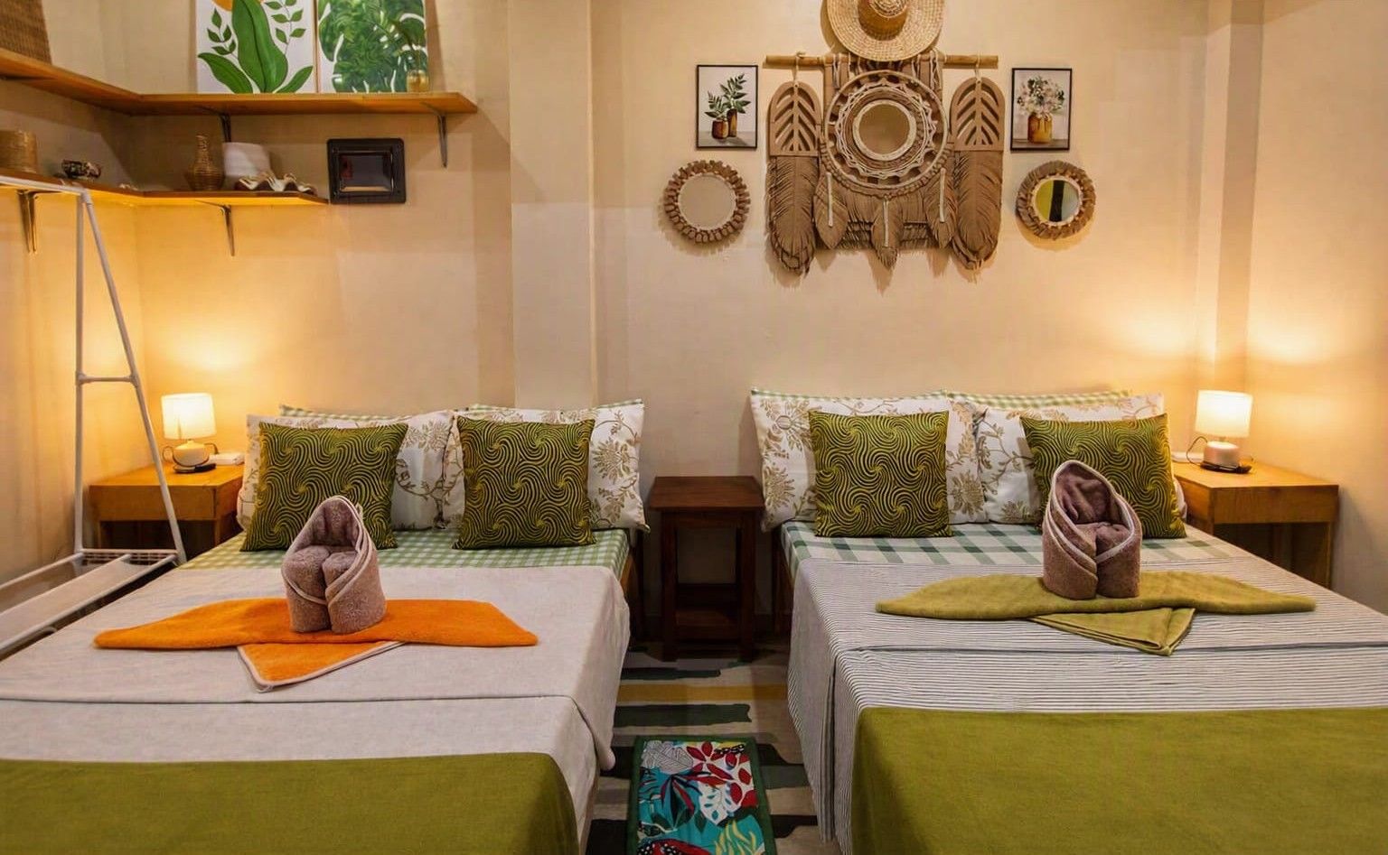 Ein Hotelzimmer mit zwei Betten, jeweils ausgestattet mit einem Kopfkissen und einem Handtuch. Es gibt ein Regal mit Dekoration und eine Wand mit gerahmten Bildern und Wandkunst.