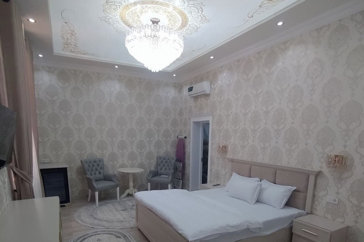 A bedroom with a large bed, bedside tables, a chair, a small table, and a chandelier.