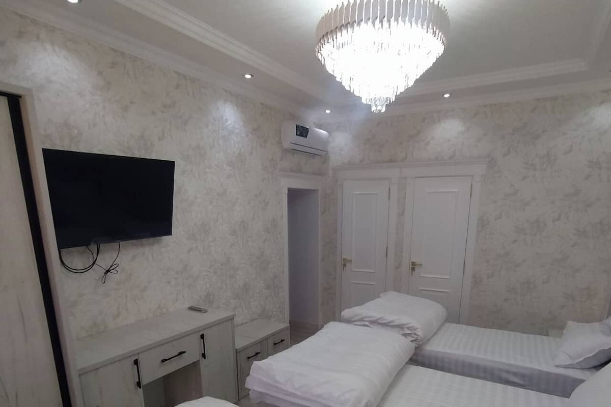 A hotel room with three beds, a TV, a wardrobe, and an air conditioning unit.