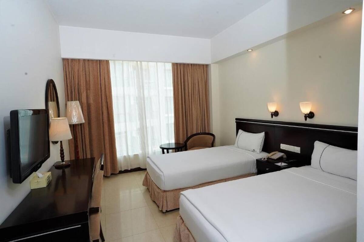 A hotel room with two beds, a desk with a lamp, a TV, and a window with curtains.