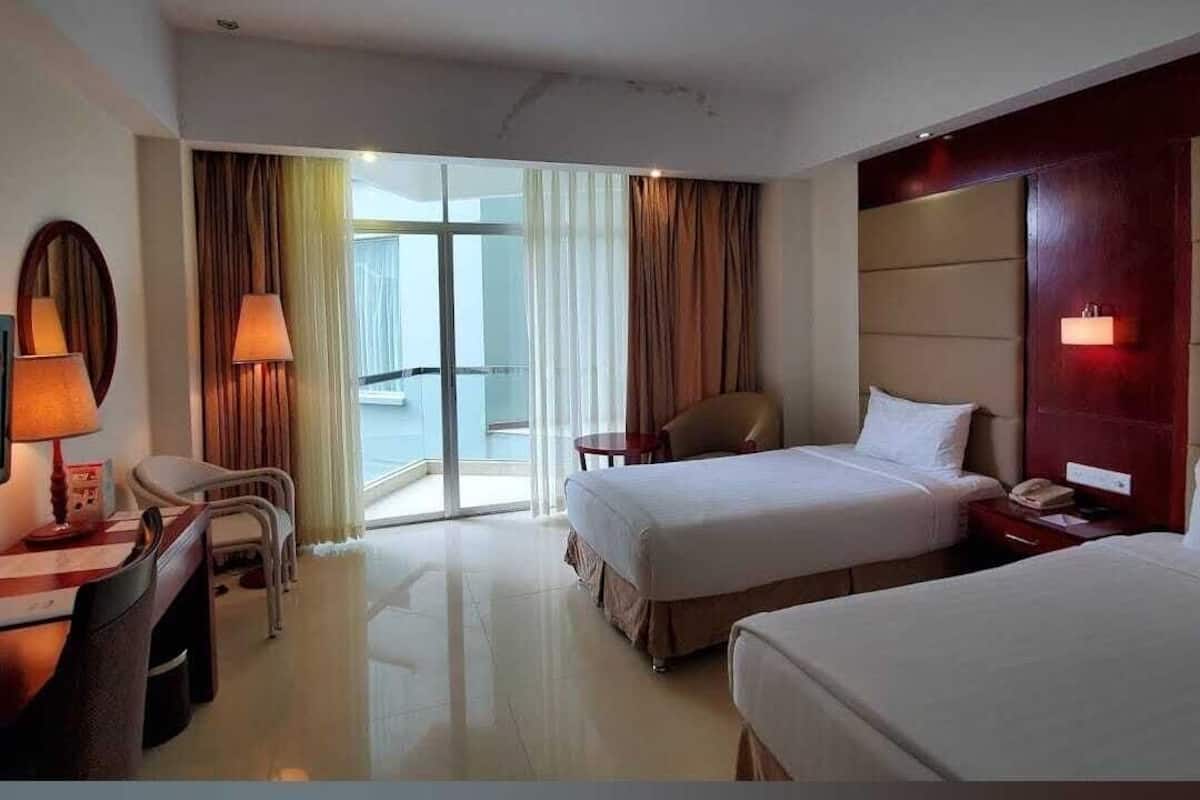 A hotel room with two beds, a desk, a chair, and a view of the outside.