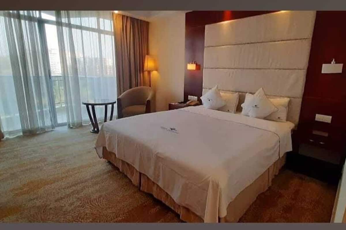 A hotel room with a large bed, a chair, a small table, and a window with curtains.