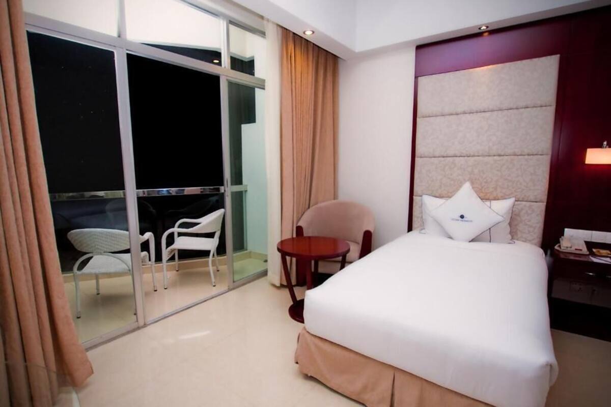 A hotel room with a large bed, a small table, two chairs, a nightstand, and a view of the outside through a glass door.