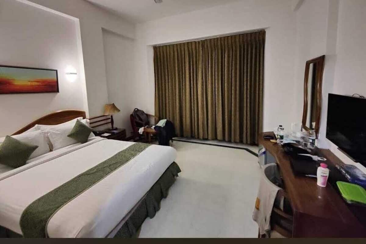 A hotel room with a bed, a desk, a chair, a television, and a window with curtains.