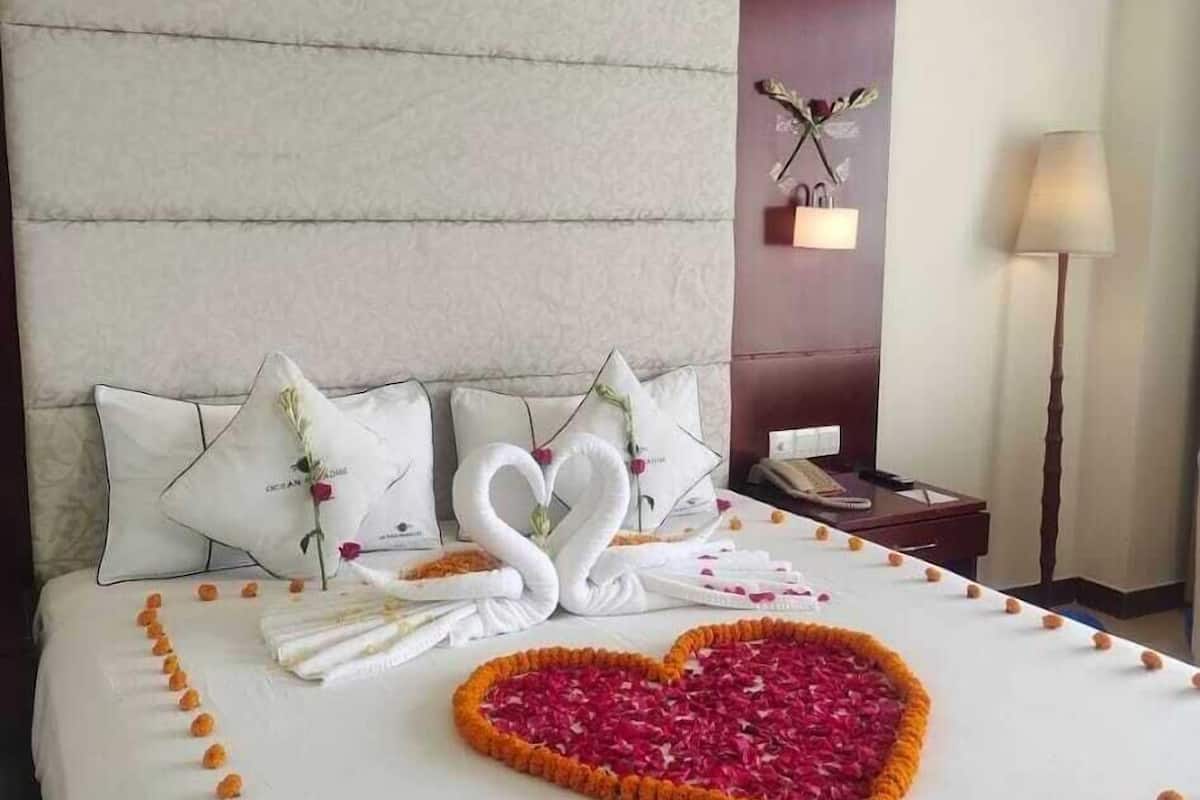 A neatly made bed with a heart-shaped flower arrangement and swan-shaped towels.