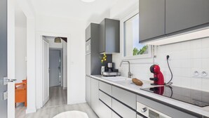 Una cocina moderna con armarios grises, encimera blanca y hervidor rojo.