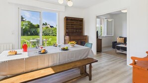 Un comedor con una mesa preparada para una comida, un banco y vistas al jardín a través de amplios ventanales.