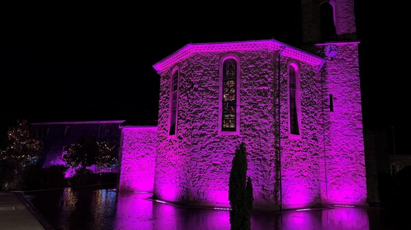 Um edifício com fachada de pedra e janelas em arco, iluminado por luzes roxas.