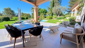 An outdoor patio with a dining table, chairs, and a sofa. There is a pool in the background.