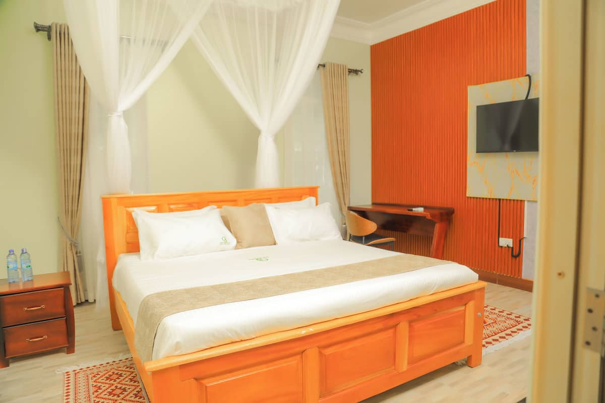 A hotel room with a wooden bed, a desk, a TV mounted on the wall, and a window with curtains.