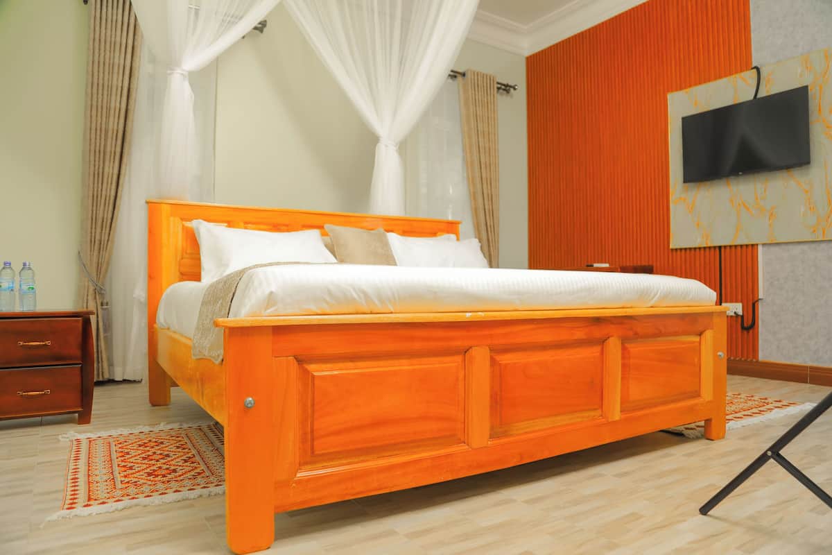 A bedroom with a wooden bed, a TV mounted on the wall, and a bedside table with bottles.