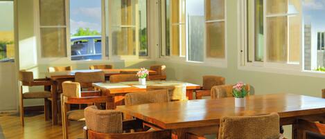 Un comedor con mesas y sillas de madera, ventanas grandes y vistas al exterior.