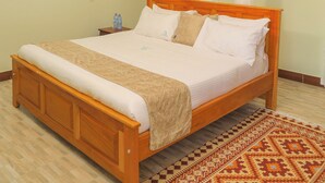 A bedroom with a wooden bed, white bedding, a patterned rug, and a canopy. - country sights Hotel Bulisa (Bulisa)