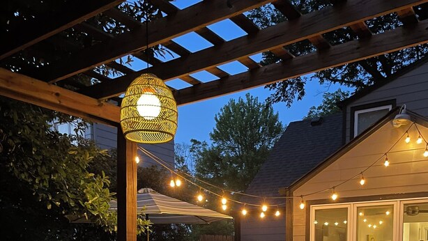 Un espace extérieur aménagé en patio, doté d’un coin salon couvert, de guirlandes lumineuses et d’une pergola.