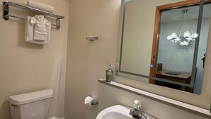 A bathroom with a toilet, sink, towel rack, and a mirror with a light above it. - Banff Woods Lodge (Harvie Heights)