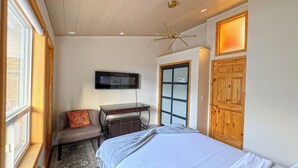 A bedroom with a bed, a desk, a chair, a television, and a large window. - Banff Woods Lodge (Harvie Heights)