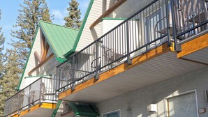 A multi-story building with a stone facade, balconies, and a green roof. - Banff Woods Lodge (Harvie Heights)