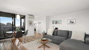 Ein modernes Wohnzimmer mit einem grauen Sofa, einem runden Glastisch und einem Essbereich mit einem Glastisch und Stühlen.