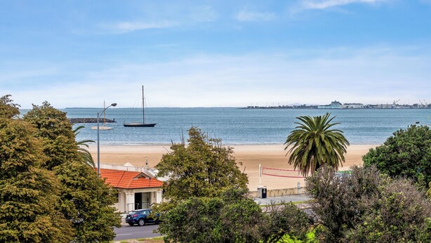 Blick auf einen Strand mit Segelboot, Palmen und einem Gebäude mit rotem Dach.