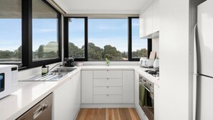 Eine moderne Küche mit weißen Schränken, einer Spüle aus Edelstahl und Blick ins Freie durch große Fenster.