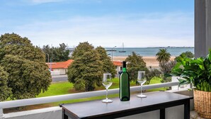 Ein Balkon mit Blick auf den Strand, eine Weinflasche und zwei Weingläser.