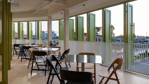 A hotel dining area with tables and chairs, large windows, and a view of the city.