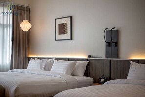 A hotel room with two beds, a bedside table, a lamp, a framed picture, and a telephone on the wall.