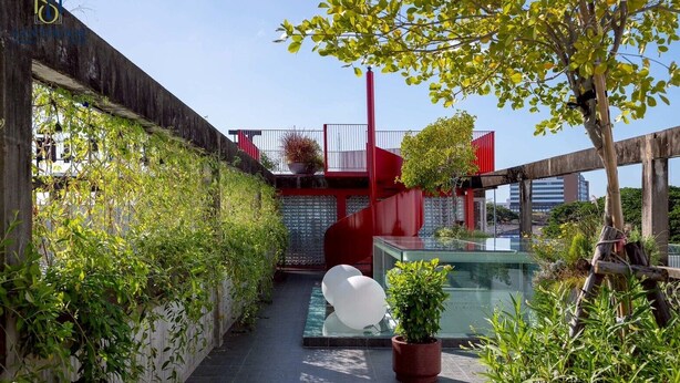 A narrow outdoor corridor with a glass-top pool, surrounded by greenery and red architectural elements.