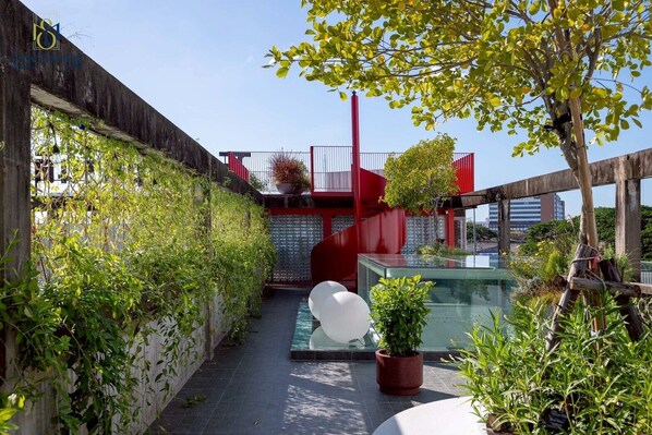 A narrow outdoor corridor with a glass-top pool, surrounded by greenery and red architectural elements.