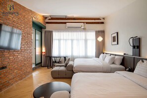 A hotel room with two beds, a TV, a brick wall, a window with curtains, and a small table with a chair. - Santisookmidtown (Pattani)