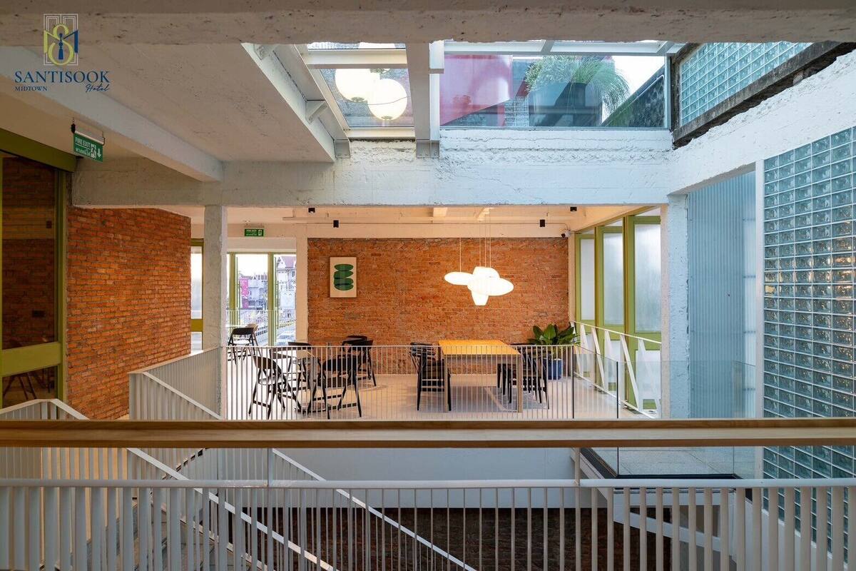 Interior del hotel Santisook en el centro, con una pared de ladrillo, una lámpara colgante y vistas de la ciudad a través de amplias ventanas.