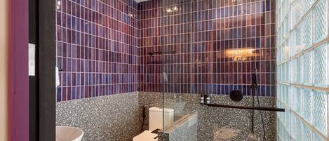 Un baño con cabina de ducha de vidrio, inodoro blanco y lavamanos de mármol.