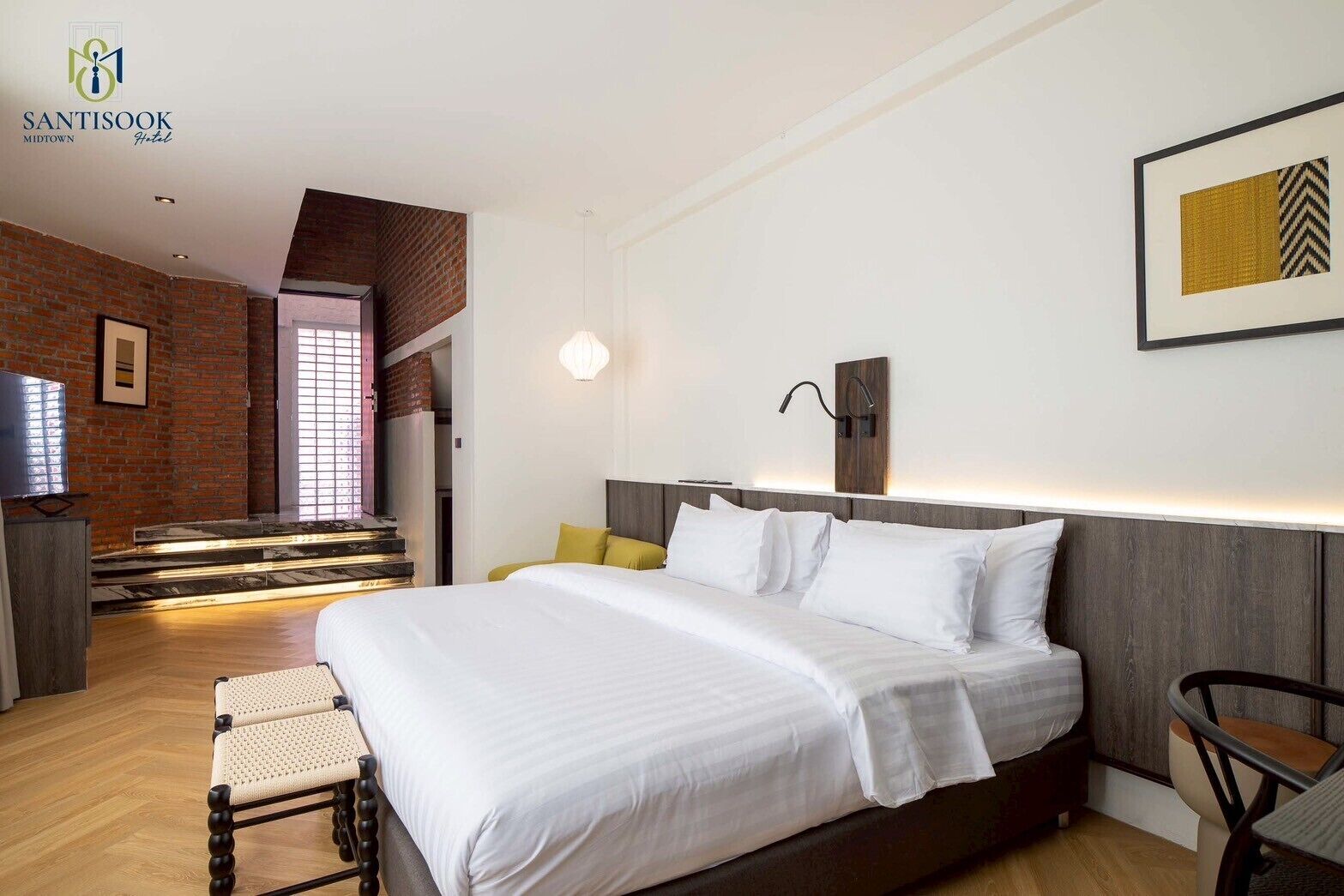 A modern hotel room with a large bed, a TV, a staircase, and a wall-mounted light fixture.