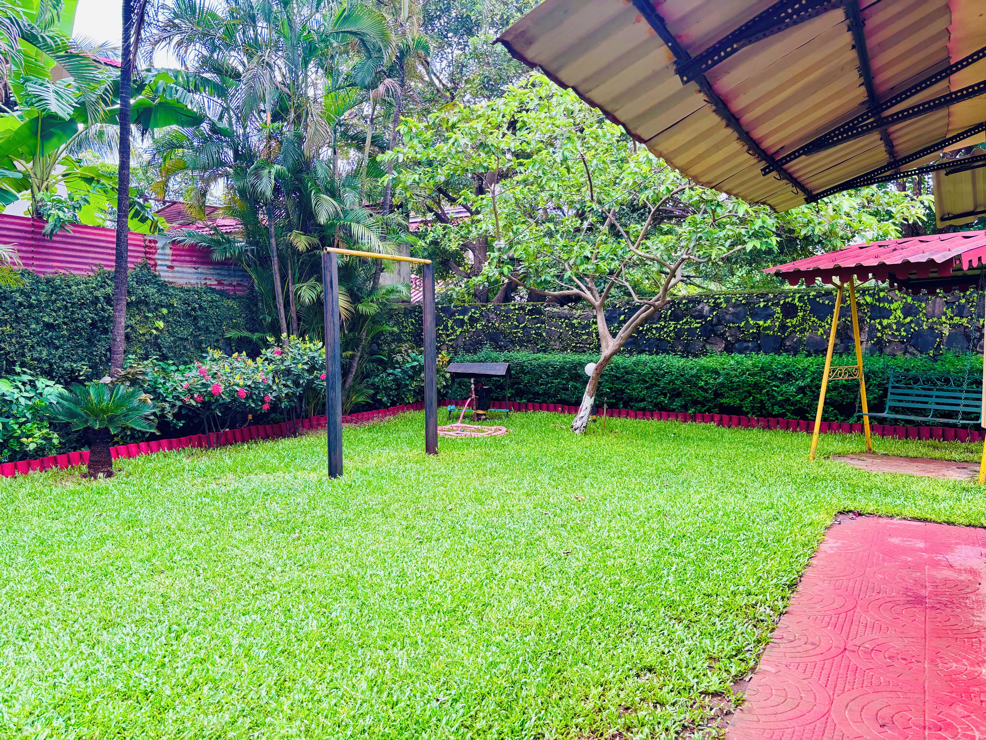 A well-maintained garden with a swing set, a covered seating area, and a stone wall.