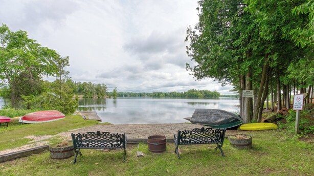 A lakeside seating area with benches and a fire pit, surrounded by trees and umbrellas.